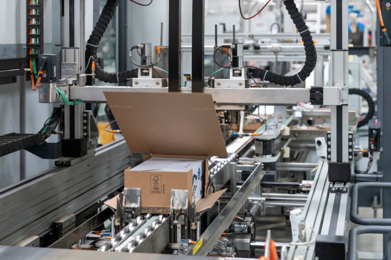 Machine d'emballage automatisée conditionnant un colis en carton sur une ligne logistique.}